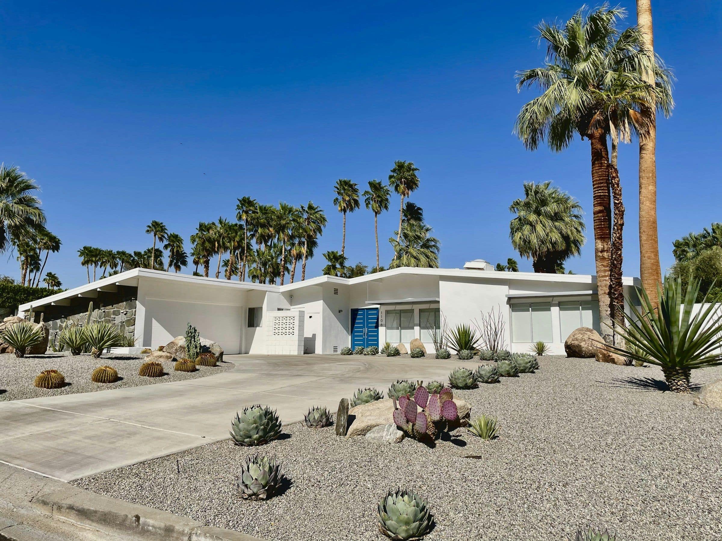 A single-storey mid-century modern home framed by palm trees and desert landscaping